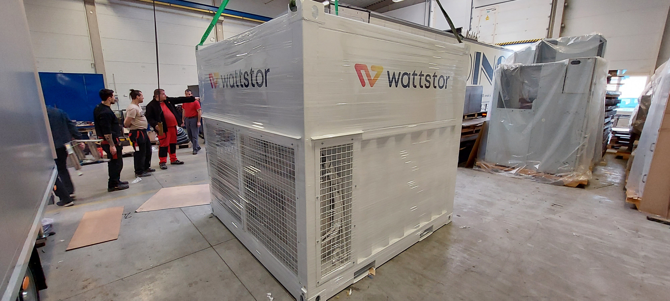 Bateriové úložiště od společnosti Wattstor pro Hrvatska Elektroprievreda v Chorvatsku, pohled na zabalené úložiště ve skladu s dělníky kolem, připraveno k přepravě.
